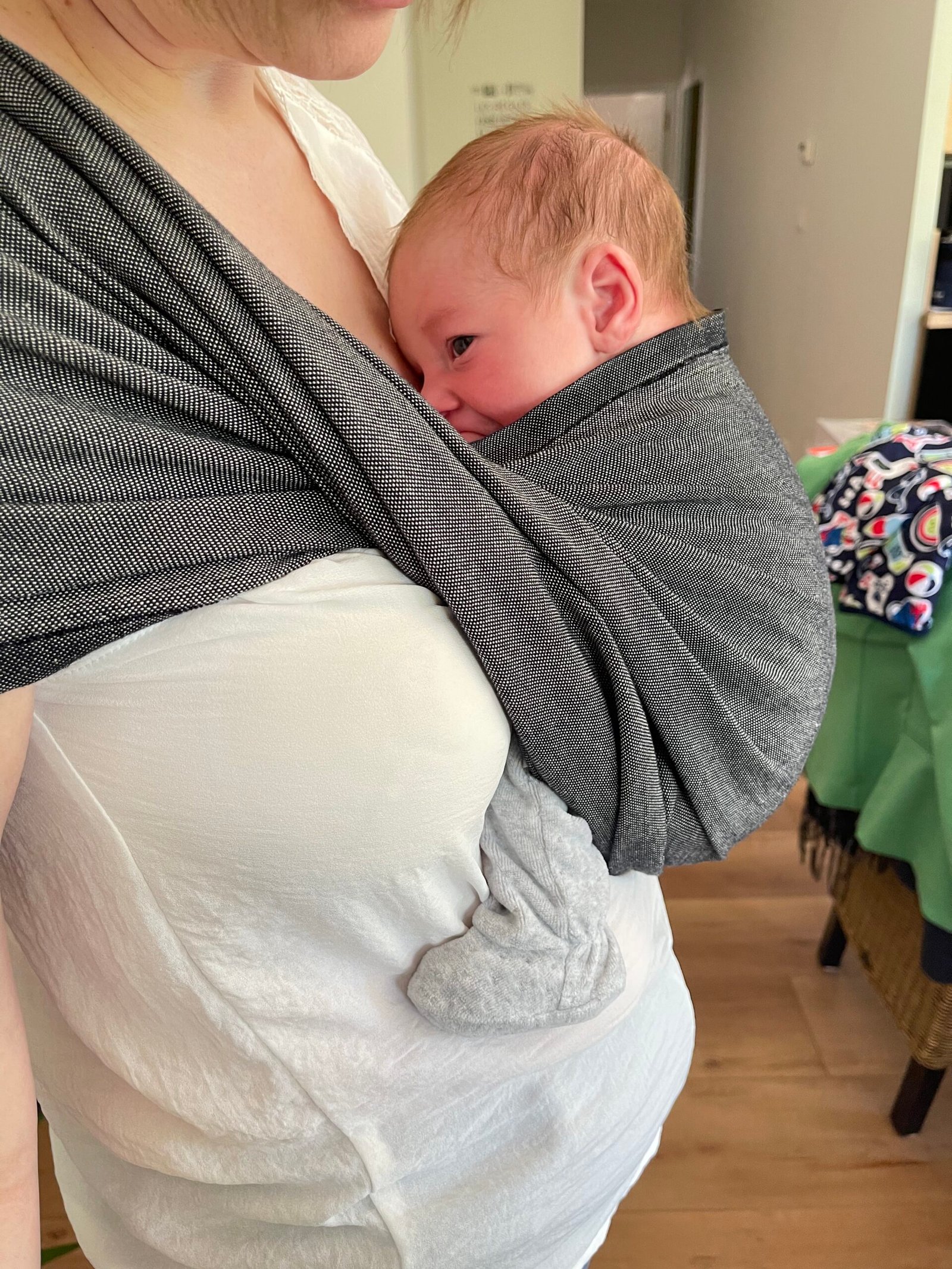 Bébé porté en sling gris contre sa maman